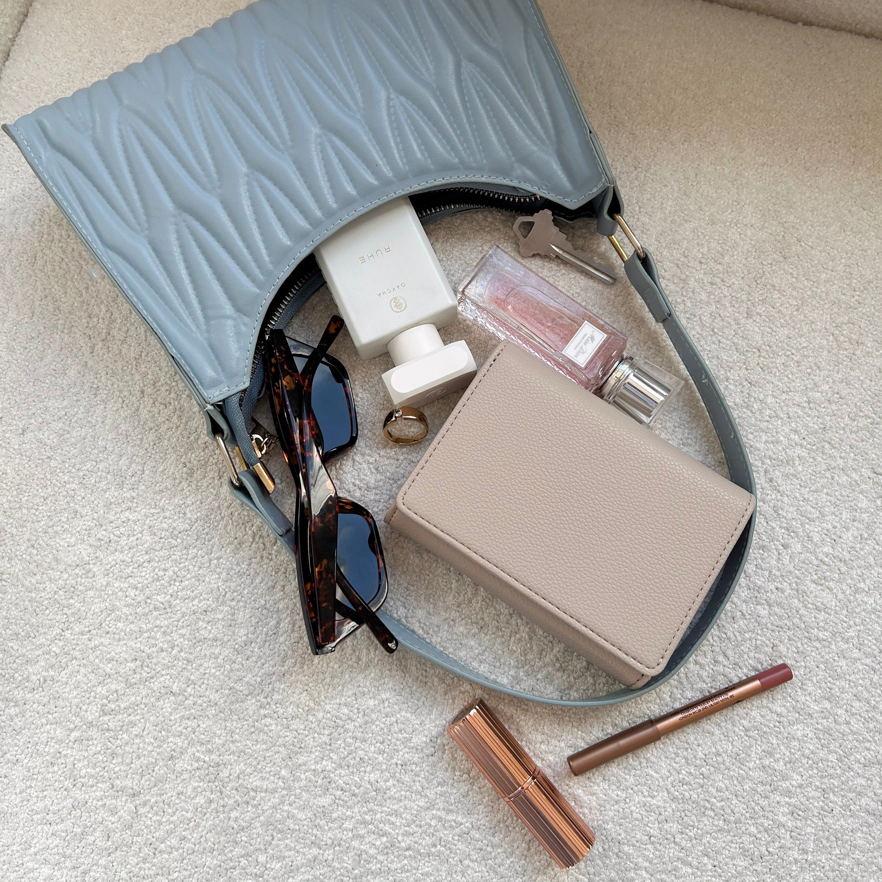Blue handbag with sunglasses, phone, and makeup items on a light surface