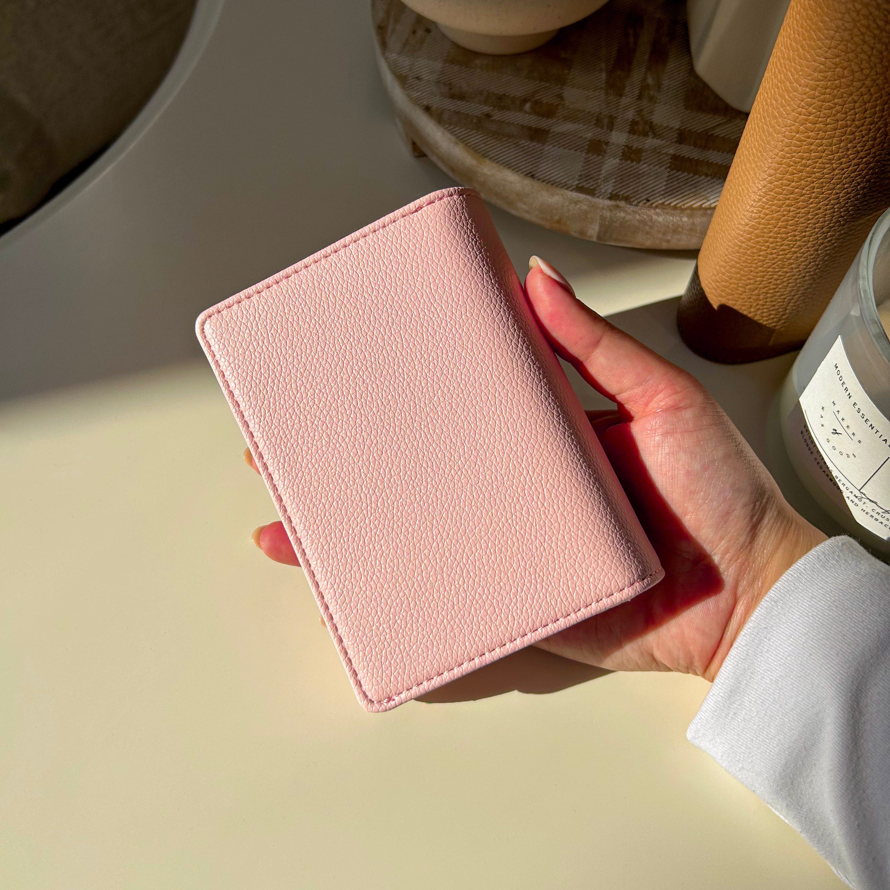 Hand holding a pink wallet on a light surface with a blurred background