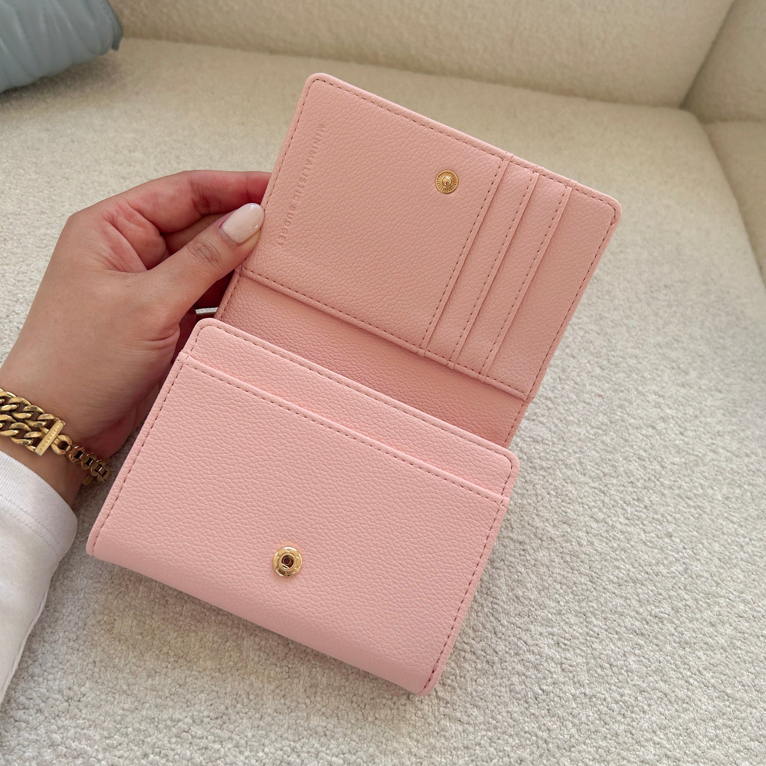 Pink wallet held open by a hand on a light-colored surface
