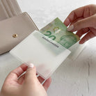 Person holding a Canadian $20 bill over an open beige wallet on a light surface.