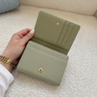 Green wallet held by a hand on a light-colored surface