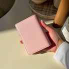 Hand holding a pink wallet on a light surface with a blurred background